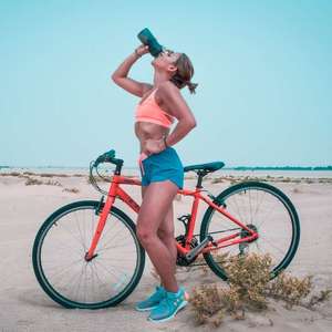 woman drinking from water bottle outside next to bike