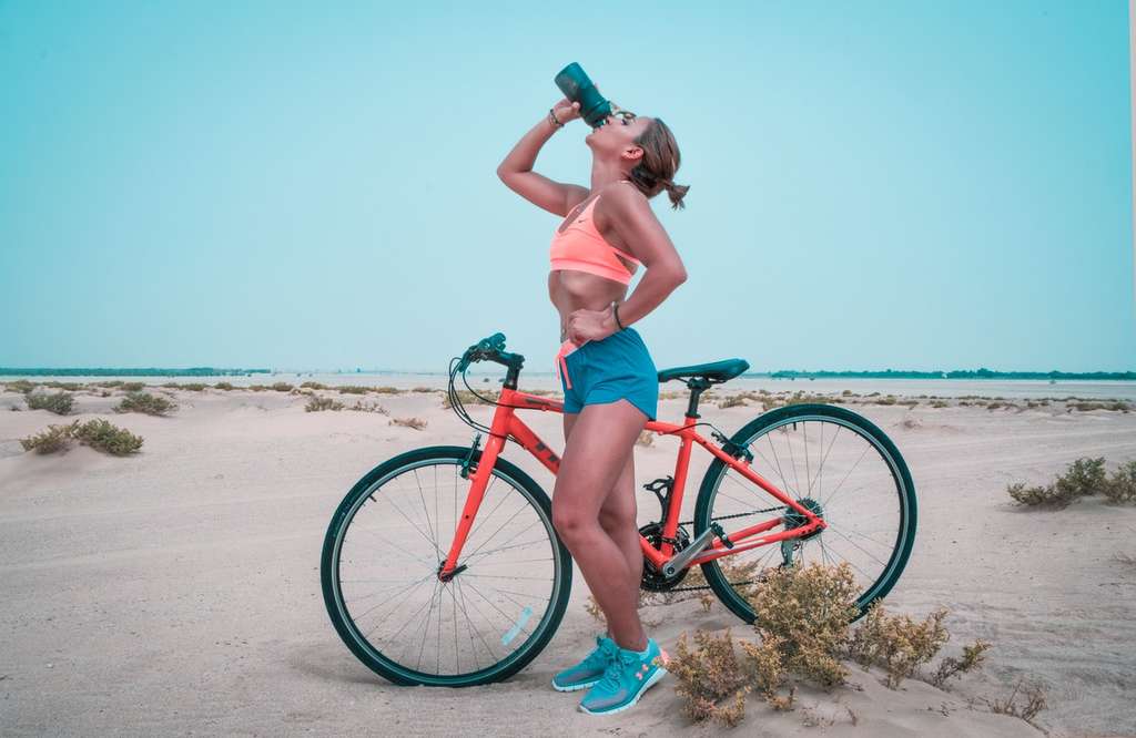 woman drinking from water bottle outside next to bike