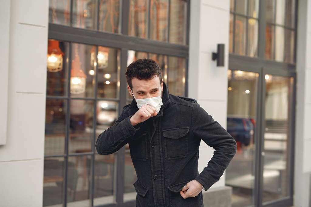 Man wearing a mask and coughing into his hand