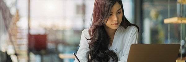 Woman looking at laptop and writing in notebook