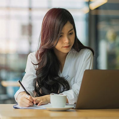 Woman looking at laptop and writing in notebook